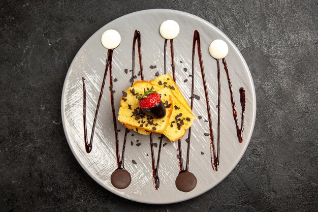 Top Nahaufnahme Dessert Kuchenstücke mit schokoladenüberzogenen Erdbeeren und Schokoladensauce auf dem grauen Teller auf dem dunklen Tisch