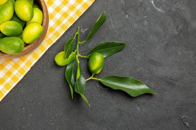 Top Nahaufnahme Früchte Früchte in der Schüssel auf der weiß-gelben Tischdecke grüne Früchte mit Blättern