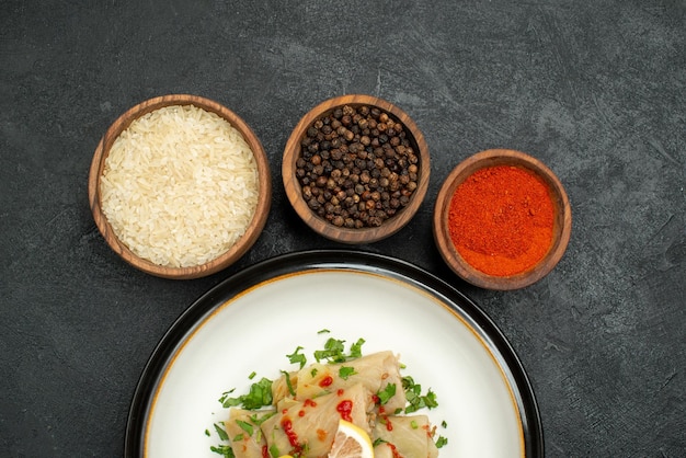 Kostenloses Foto top nahaufnahme gericht mit gewürzen appetitlich gefüllten kohl mit kräutern zitrone und sauce und schalen mit bunten gewürzen reis und schwarzem pfeffer auf dunkler oberfläche