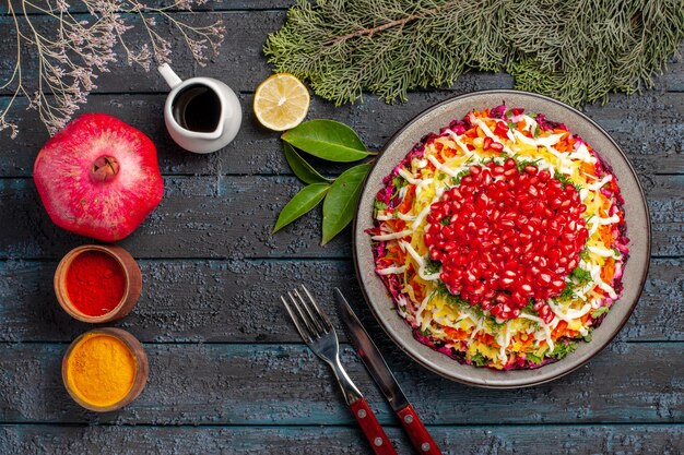 Kostenloses Foto top-nahaufnahme-gericht mit granatapfel-gericht mit granatäpfeln neben dem granatapfel-zitronen-gewürzmesser und gabel-fichtenzweigen