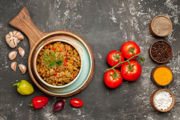 Top Nahaufnahme grüne Bohnen weiße Notizbuchplatte der grünen Bohnen mit Tomaten auf dem Brett Paprika Zwiebel Knoblauch Tomaten mit Stiel und bunten Gewürzen auf dem dunklen Tisch