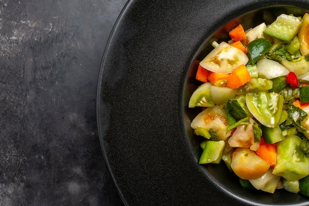 Top Nahaufnahme grüner Tomatensalat auf schwarzem ovalen Teller auf dunklem Hintergrund