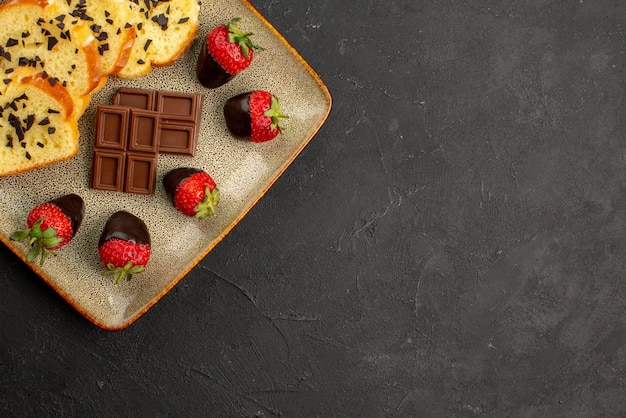 Top Nahaufnahme Kuchen auf Teller leckerer Kuchen mit schokoladenüberzogenen Erdbeeren und Schokolade auf dem quadratischen grauen Teller auf der linken Seite des Tisches