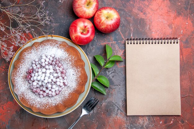 Top Nahaufnahme Kuchen ein appetitlicher Kuchen mit Beeren Gabel Äpfel Blätter weißes Notizbuch