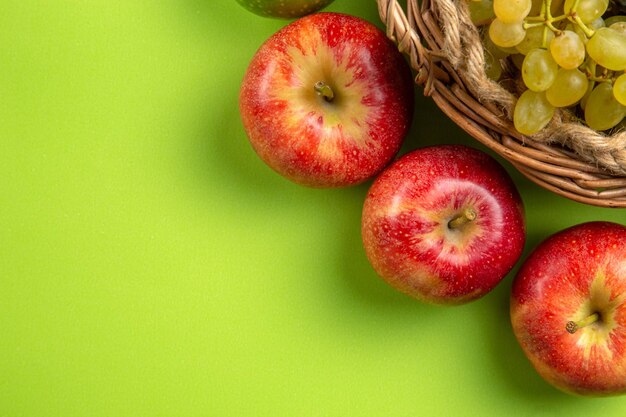 Top Nahaufnahme Obstkorb mit grünen Trauben drei rote Äpfel auf dem grünen Hintergrund