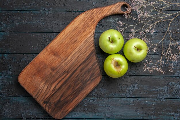 Top Nahaufnahme Äpfel und Board drei grüne Äpfel neben Küchenbrett und Ästen auf dunkler Oberfläche