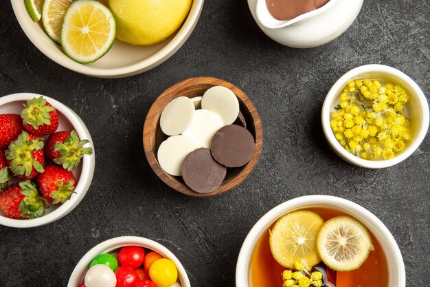 Top Nahaufnahme Schokoladen- und Erdbeerschalen mit Schokoladenkräutern und Erdbeeren neben der Tasse Kräutertee auf dem dunklen Tisch