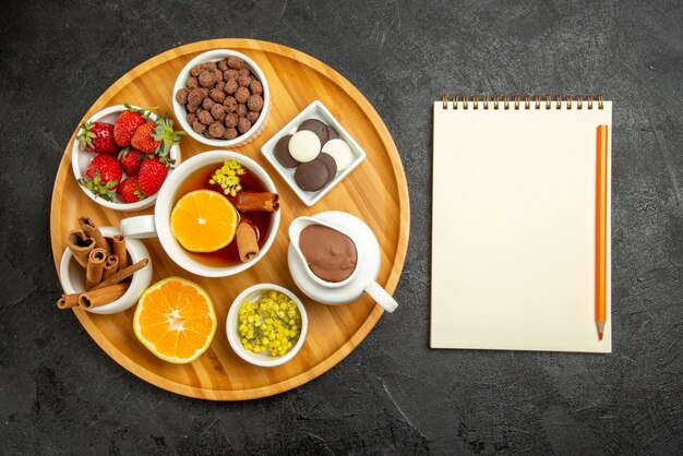 Top Nahaufnahme Süßigkeiten auf Tischplatte mit Schokoladenbeeren Zitronen-Zimt-Sticks und eine Tasse Tee mit Zitrone neben dem weißen Notizbuch mit gelbem Bleistift