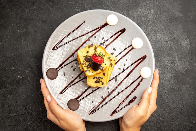 Top Nahaufnahme Süßigkeiten Teller Kuchen mit schokoladenüberzogenen Erdbeeren und Schokoladensauce in den Händen