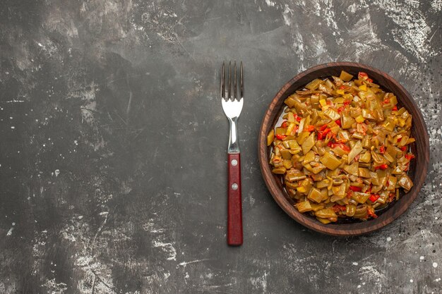 Top Nahaufnahme Teller mit grünen Bohnen brauner Teller der appetitlichen grünen Bohnen und Tomaten neben der Gabel auf der rechten Seite des dunklen Tisches