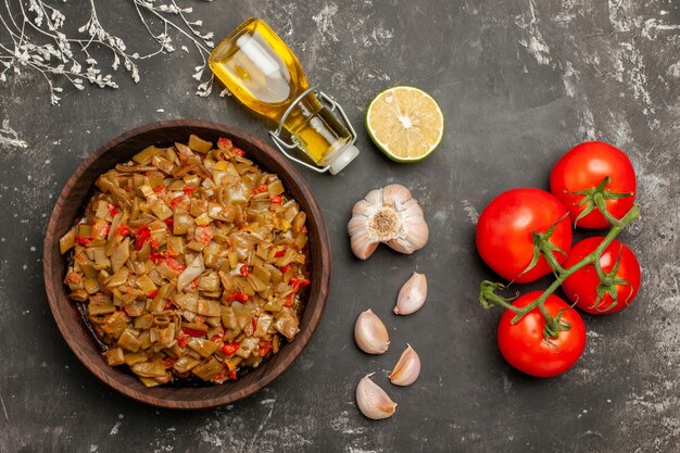 Top Nahaufnahme Teller mit grünen Bohnen Flasche Öl Knoblauch Zitrone neben den reifen roten Tomaten mit Pedikel Teller mit grünen Bohnen und Tomaten auf dem Tisch