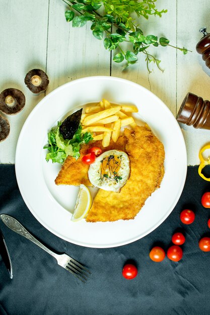 Top paniertes Hähnchenfilet serviert mit Pommes Frites Spiegelei und Kirschtomaten auf Teller