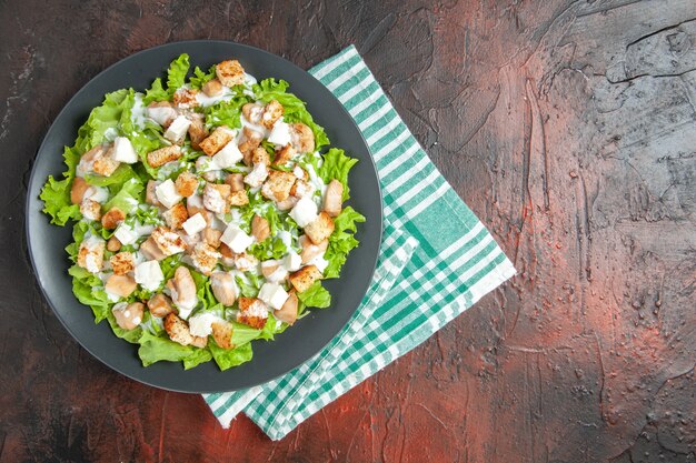 Top-View Caesarsalat auf einem ovalen Teller grün-weiß gerahmte Serviette auf dunkelrotem Hintergrund