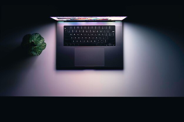Top-View eines Laptops auf einem Tisch, der im Dunkeln auf dem Bildschirm leuchtet