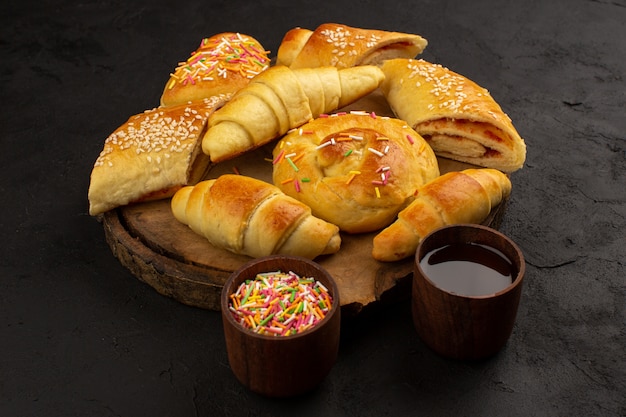 Top View Gebäck zusammen mit Croissants lecker süß auf dem braunen Schreibtisch und dunklem Boden