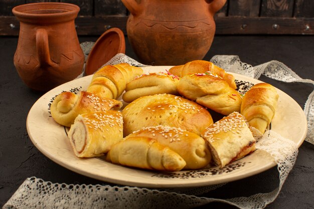 Top View Gebäck zusammen mit leckeren Croissants in weißen Teller auf dem dunklen Boden