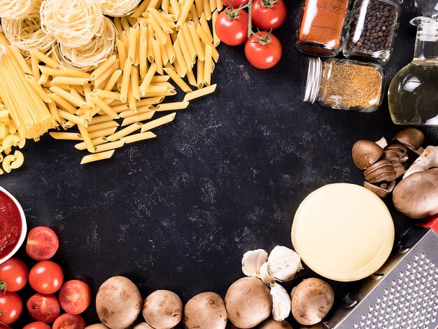 Top-View-Mix aus ungekochten rohen Nudeln, Spaghetti, Makkaroni neben Pilzen, Käse, Tomatensoße, frischen Tomaten, Gewürzen und Sonnenblumenöl. Exemplar verfügbar