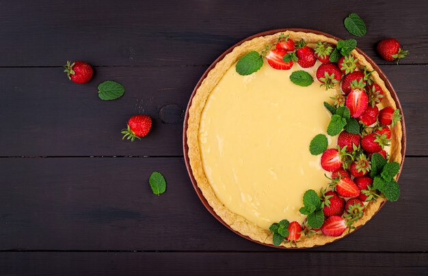 Torte mit Erdbeeren und Schlagsahne, dekoriert mit Minzblättern auf dunklem Tisch. Draufsicht