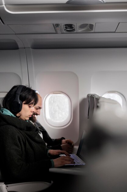 Touristen paar arbeiten am Laptop und benutzen Handy während des kommerziellen Fluges im Flugzeug. Menschen, die mit einer internationalen Fluggesellschaft zum Urlaubsziel reisen und ins Ausland fliegen.
