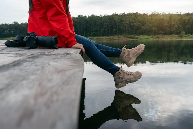 Kostenloses Foto touristen schwingen die füße in der nähe der wasseroberfläche, frau entspannt sich am see und sitzt auf einem holzsteg.