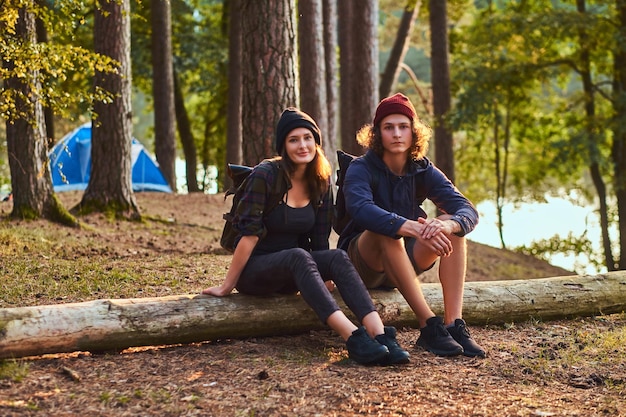 Touristenmädchen hält die Hand am Kinn, während sie auf einem Baumstamm sitzt und hält ein Smartphone im Wald.