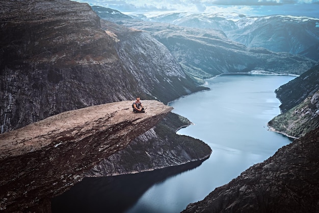 Kostenloses Foto touristenmann sitzt in der trolltunga und genießt die schöne aussicht auf den norwegischen fjord.