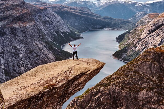 Touristenmann steht in der Trolltunga und genießt die schöne Aussicht auf den norwegischen Fjord.