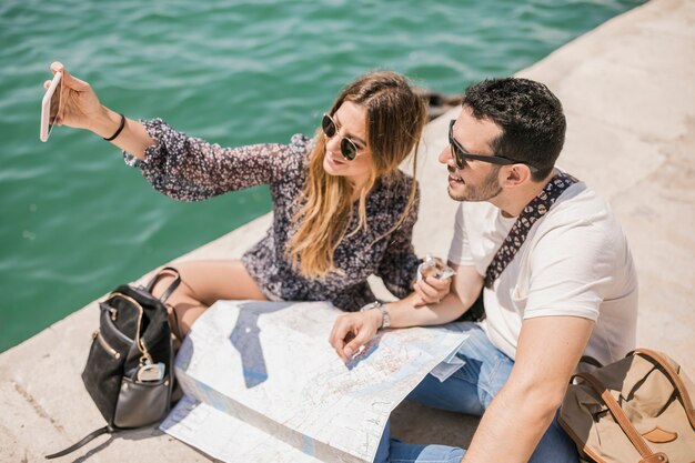 Touristische Paare, die auf ansteckendem Selbstporträt der Anlegestelle am Handy sitzen