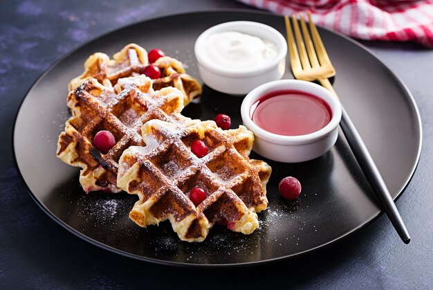 Traditionelle belgische Waffeln mit Beeren, Sauerrahm und Marmelade auf dunklem Tisch.