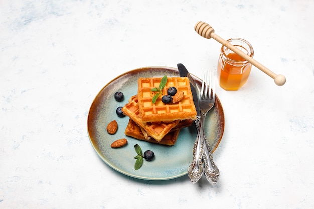 Traditionelle belgische Waffeln mit frischen Beeren und Honig auf grauer Betonoberfläche.