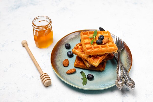 Traditionelle belgische Waffeln mit frischen Beeren und Honig auf grauer Betonoberfläche.