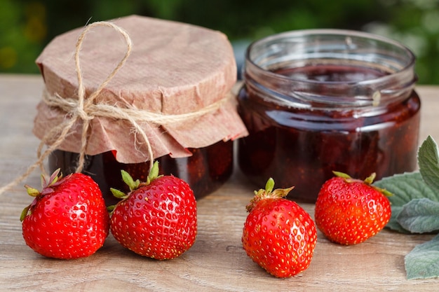 Traditionelle hausgemachte erdbeermarmelade in gläsern mit frischen erdbeeren auf holztisch Premium Fotos