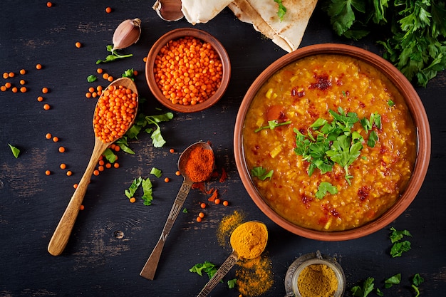 Traditionelle indische Suppenlinsen. Indian Dhal würziges Curry in Schüssel, Gewürzen, Kräutern, rustikalem schwarzem Holztisch