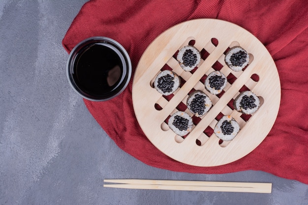 Kostenloses Foto traditionelle maki-sushi-rolle mit stäbchen und sojasauce auf roter tischdecke.