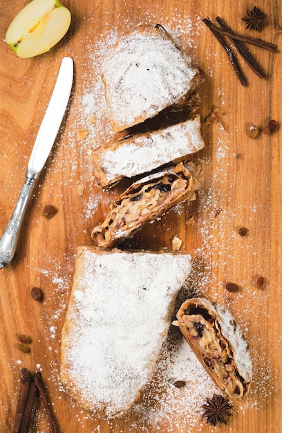 Traditioneller österreichischer Apfelkuchen - Apfelstrudel mit Äpfeln, Nüssen, Zimt und Rosinen, in Scheiben geschnittener Strudel auf einem Holzschneidebrett, Draufsicht.