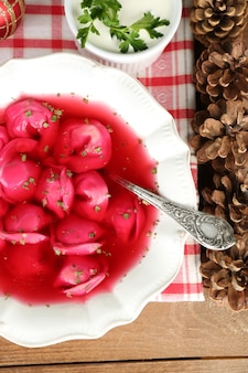 Traditioneller polnischer klarer roter borschtsch mit knödeln in schüssel auf tablett und weihnachtsschmuck auf holzoberfläche