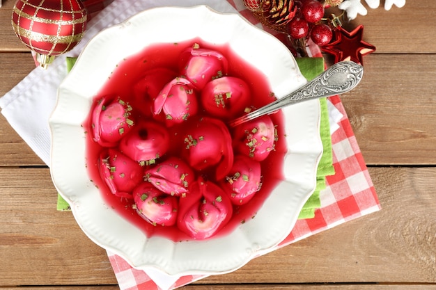 Traditioneller polnischer klarer roter borschtsch mit knödeln und weihnachtsdekorationen auf holztischhintergrund