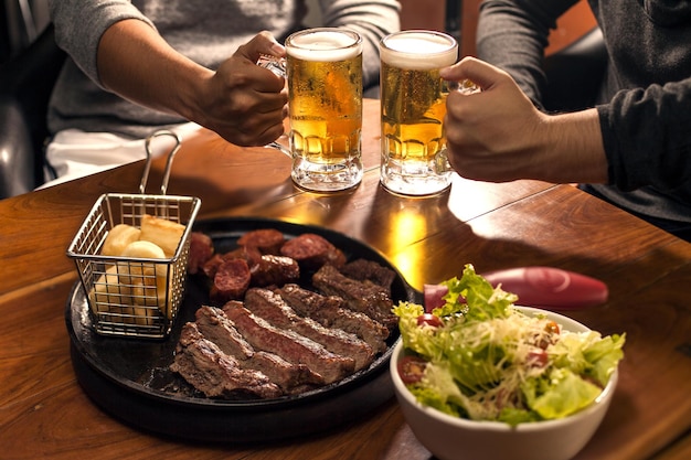 Kostenloses Foto traditionelles argentinisches grillfleisch und salat mit menschen, die im hintergrund bier trinken