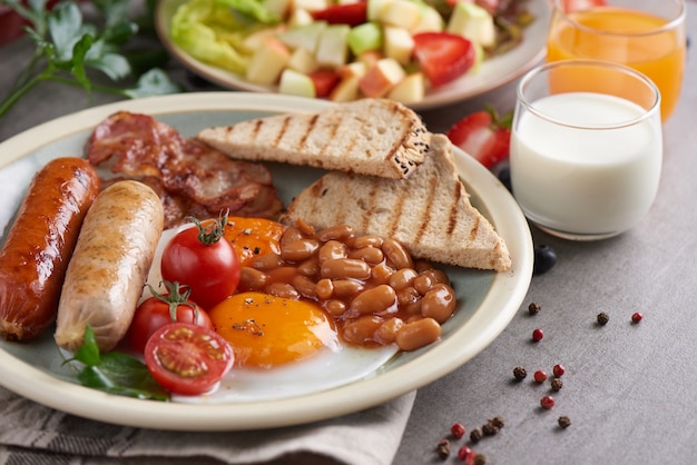 Traditionelles englisches Frühstück mit Spiegeleiern, Wurst, Tomaten, Bohnen, Toast und Speck auf einem Teller