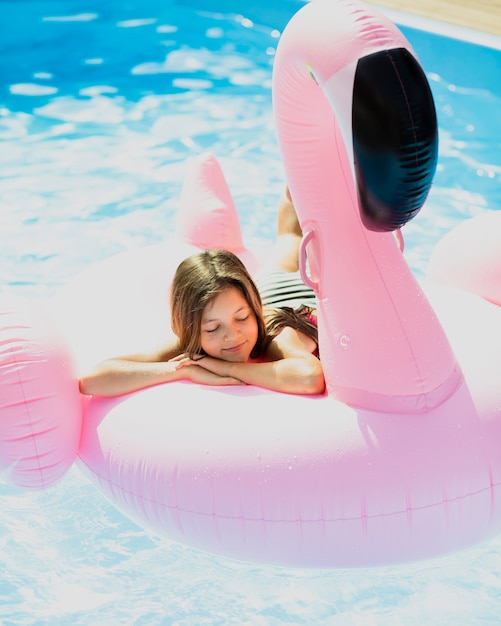 Träumerisches Mädchen, das auf einem Flamingofloatie sitzt