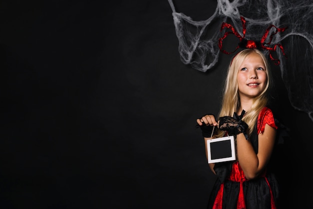 Träumerisches Mädchen in Halloween-Kostüm, das Tafel hält