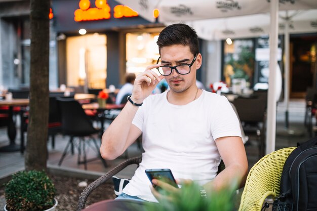 Tragende Brillen des Mannes unter Verwendung des Mobiltelefons