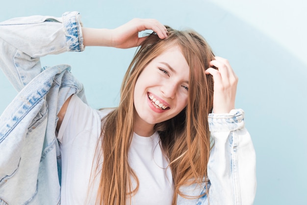 Tragende Denimjacke der glücklichen attraktiven Frau, die nahe blauem Hintergrund aufwirft