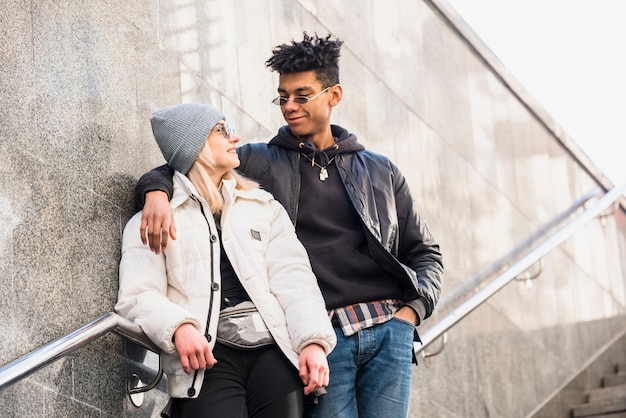 Tragende Sonnenbrille der modernen zwischen verschiedenen Rassen jungen Paare, die auf dem Treppenhaus betrachtet einander steht