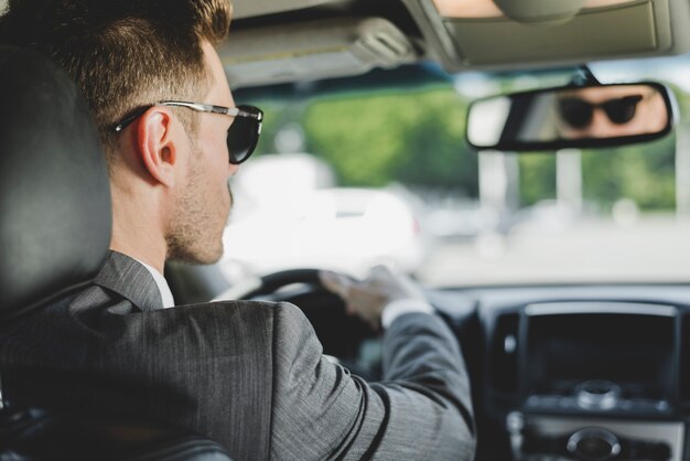 Tragende Sonnenbrille des gutaussehenden Mannes, die Rückspiegel im Auto betrachtet