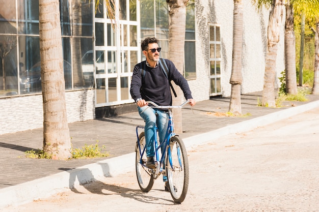 Tragende Sonnenbrille des modernen Mannes, die Fahrrad auf Straße fährt