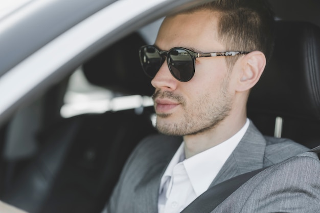 Tragende Sonnenbrille des stilvollen jungen Geschäftsmannes, die Auto fährt