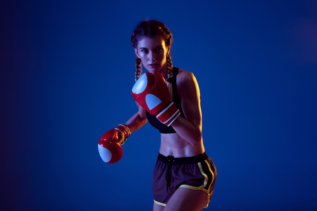 Trainieren. Passende kaukasische Frau im Sportbekleidungsboxen auf blauem Hintergrund im Neonlicht.