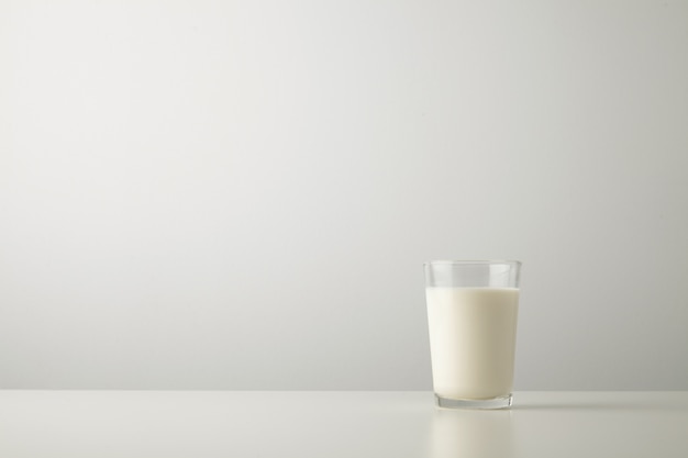 Transparentes Glas mit frischer Bio-Milch lokalisiert auf der Seite des weißen Tisches. Platz für Ihren Text oben