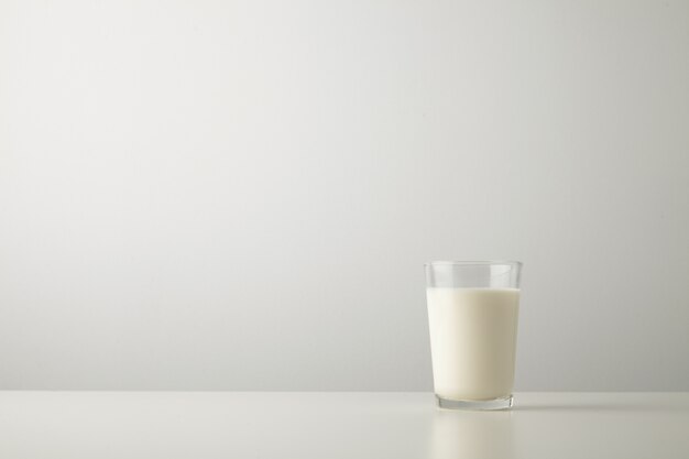 Transparentes Glas mit frischer Bio-Milch lokalisiert auf der Seite des weißen Tisches. Platz für Ihren Text oben